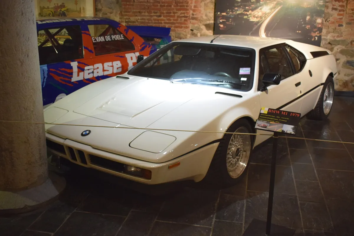 The white 1979 BMW M1 on display in the Spa-Francorchamps Circuit Museum, with its 'BMW M1 1979' plaque and an E30 BMW M3 racing car behind it